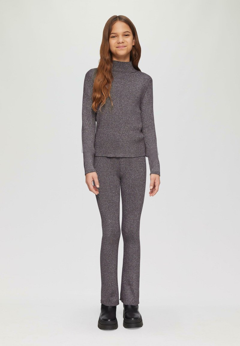 Pull en maille côtelée gris avec pantalon assorti et col montant, présentant un subtil éclat. Porté avec des bottes à semelle épaisse noires.