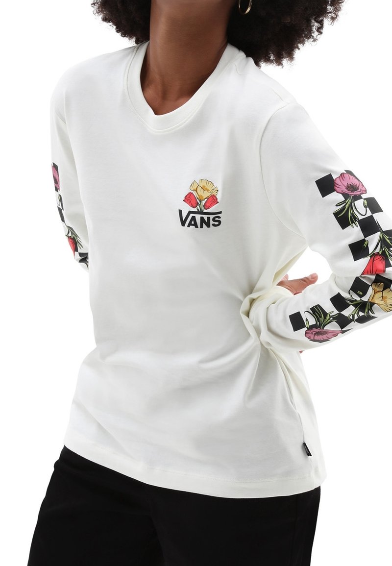 Witte langslijf t-shirt met bloemmotieven en een schaakbordpatroon op de mouwen. Gemaakt van zachte katoenstof. Logo op de voorkant.