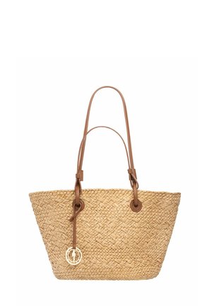 Tkana słomiana torba na ramię z dwoma jasnobrązowymi skórzanymi uchwytami i skórzanym paskiem trzymającym z przodu okrągły złoty wisiorek.