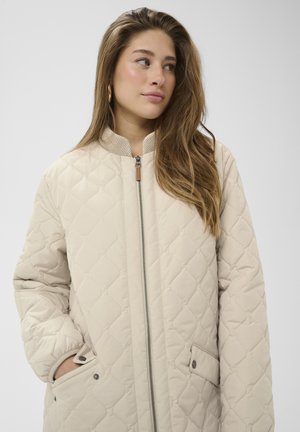 Svetlo bež prešita jakna z rebrastim ovratnikom, z zadrgo in stranskimi žepi s pritisnimi gumbi; gladka tekstura s kvadratnim krojem.