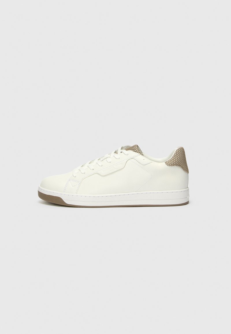 Λευκά δερμάτινα sneakers με μια υφασμάτινη μπεζ επένδυση στην φτέρνα. Διαθέτουν στρογγυλά κορδόνια, καουτσούκ σόλα και μινιμαλιστικές σχεδιαστικές λεπτομέρειες.