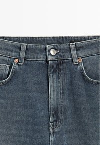 Džíny z denimu s tmavě modrým přelivem, s kovovým knoflíkem a nýty, pětikapsovým designem a kontrastním šitím.