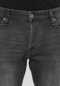 Jeans de mezclilla negra con un diseño ajustado, cierre de botón metálico y estilo de cinco bolsillos. La tela tiene una textura suave con un ligero desvanecimiento.