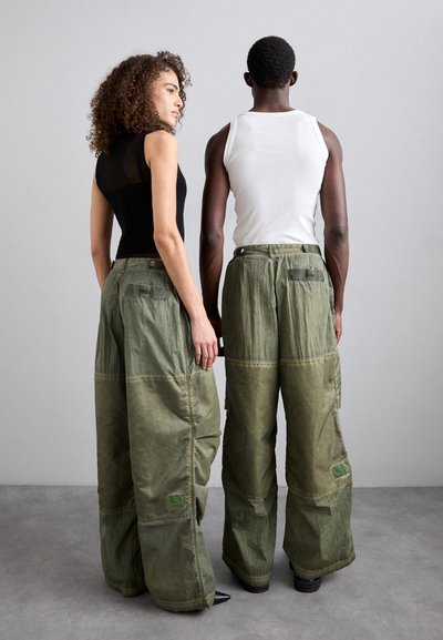 Übergroße grüne Cargo-Hosen mit Patchwork-Design, die große Taschen und sichtbare Nähte aufweisen, getragen von zwei Personen von hinten.
