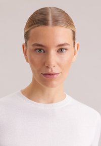 Maglione bianco lavorato a maglia con scollo rotondo, caratterizzato da una texture liscia. Lo scollo presenta una finitura a costine, che valorizza il design semplice.