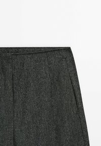 Harmaat housut, joissa on kalanruotokuvio ja laskostettu etuosa, sileä pinta ja vyölenkki, sopii muodollisiin tilaisuuksiin.