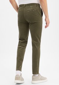 Oliwkowe spodnie kordowe o dopasowanym kroju, z tylnymi kieszeniami i mankietami, w zestawieniu z jasnymi trampkami.