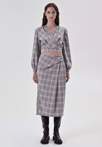 Crop top grigio a scacchi con maniche lunghe abbinato a una gonna a portafoglio coordinata e stivali neri lucidi al ginocchio. Tessuto dalla texture morbida.