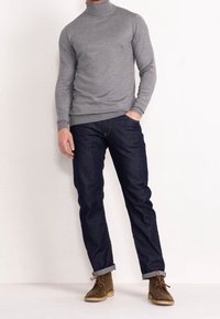 Pull à col roulé gris, jean en denim foncé avec ourlets retroussés, et bottes en daim marron. Design simple avec une coupe ajustée et une texture douce.