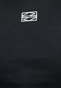 Μαύρο ριμπ ύφασμα με μικρό άσπρο κεντητό αφηρημένο γεωμετρικό λογότυπο στο κέντρο κοντά στο επάνω μέρος.