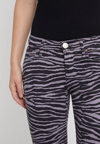 Jeans ajustados en púrpura con un patrón de rayas de tigre negras, que cuentan con bolsillos frontales, un cierre de botón y una textura de denim ligeramente elástica.