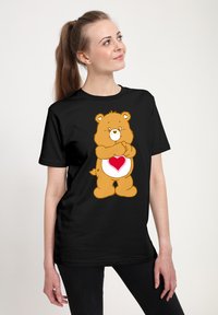 Camiseta negra con un oso de dibujos animados que tiene un patrón de corazones en su vientre. El oso es marrón, con una cara y acentos de color crema.