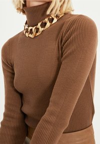 Suéter marrón de cuello vuelto acanalado con mangas largas y un alto cuello, combinado con un collar de cadena gruesa dorada.