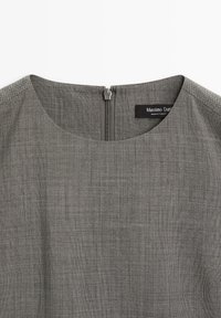 Graues, gewobenes Kleid mit rundem Ausschnitt, rückseitigem Reißverschluss und Etikett. Der Stoff hat ein strukturiertes, dezentes Muster.