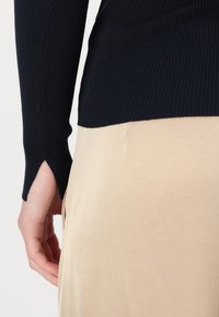 Navy ribbed sweater with side slit hem adjacent to a smooth, beige skirt. Sweater features fitted long sleeves and a textured design.