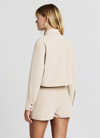 Giacca in velluto a coste beige chiaro con collo alto e design corto, abbinata a pantaloncini coordinati. Presenta maniche lunghe e dettagli con bottoni.