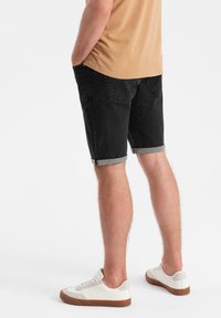 Pantalones cortos de mezclilla negra con dobladillos enrollados, combinados con zapatillas blancas que tienen un acento gris claro. La camiseta es de un color marrón sólido.