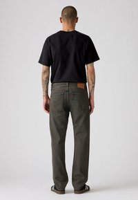 Zwarte t-shirt en donkergrijze spijkerbroek met een losse pasvorm, met een leren patch op de achterkant en decoratieve stiksels op de zakken.