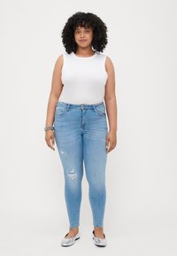 White sleeveless top, light blue skinny jeans featuring distressed areas, and silver flats. Plain background.