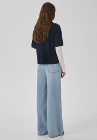 Marineblaues Kurzarmoberteil kombiniert mit weit geschnittenen hellblauen Jeans. Das Outfit wird durch ein kontrastierendes weißes Langarmshirt darunter ergänzt.