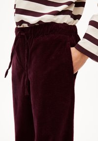 Burgunderfarbene Cord-Hose mit einem elastischen Bund und Kordelzug, ausgestattet mit Seitentaschen und einer weich strukturierten Oberfläche.