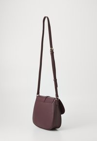 Sac en cuir bordeaux porté en bandoulière avec une forme élégante et arrondie. Dispose d'une sangle réglable et d'une fermeture à rabat, texture lisse, quincaillerie minimale.