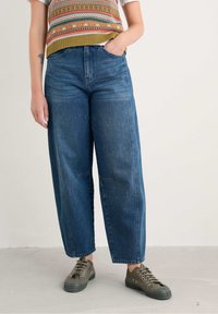 Wijd pijpen blauwe jeans met een hoge taille, voorzien van vo pockets en een vervaagde afwerking. In combinatie met olijfgroene vetersneakers.