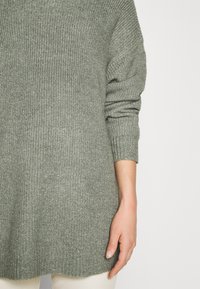 Suéter de punto verde con un corte holgado, mangas acanaladas y dobladillo redondeado. La textura es suave y ligera con un patrón delicado.