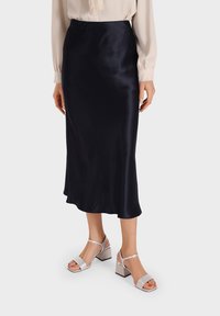 Gonna midi in satin blu navy con una texture liscia e orlo fluente, abbinata a sandali con tacco blocco argentati adornati con strass.