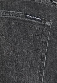 Mörkgrå denimjeans med en texturerad yta, med en bakficka och en Calvin Klein Jeans etikett sydd på fickan.