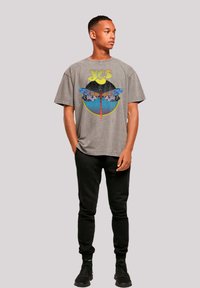 Gray oversized t-shirt with colorful dragonfly graphic and moon design, paired with black jogger pants and dark sneakers.