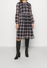 Pitkähihaista ruudullista mekkoa tummansinisenä, kermanvärisenä ja beigeinä. Ominaisuuksina kerätty vyötärö, frillalahelmus ja nauhat kaula-aukolla. Yhdistetty polvisukkiin mustilla saappailla.