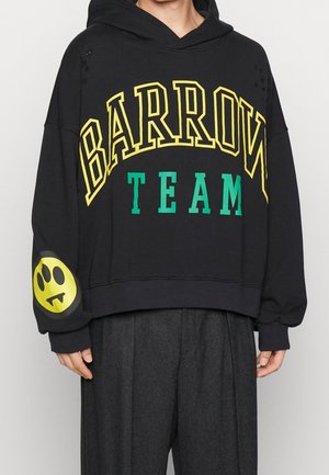 Schwarzer oversized Hoodie mit gelbem "BARROW"- und grünem "TEAM"-Schriftzug, mit einem gelben Smiley mit Vampirzähnen am linken Ärmel.