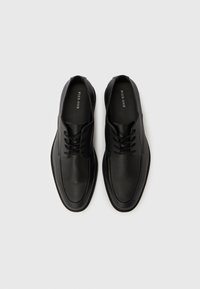 Μαύρα δερμάτινα παπούτσια με κορδόνια, λείο φινίρισμα, στρογγυλή μύτη και μινιμαλιστικό σχέδιο. Ελαστική σόλα και ομαλή υφή. Όνομα μάρκας στο εσωτερικό.