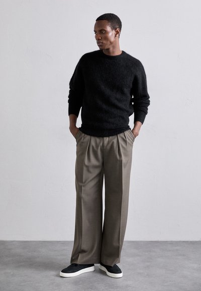 Suéter negro y difuso, pantalones beige holgados con pliegues y zapatillas negras con suelas blancas. Diseño simple, materiales texturizados.
