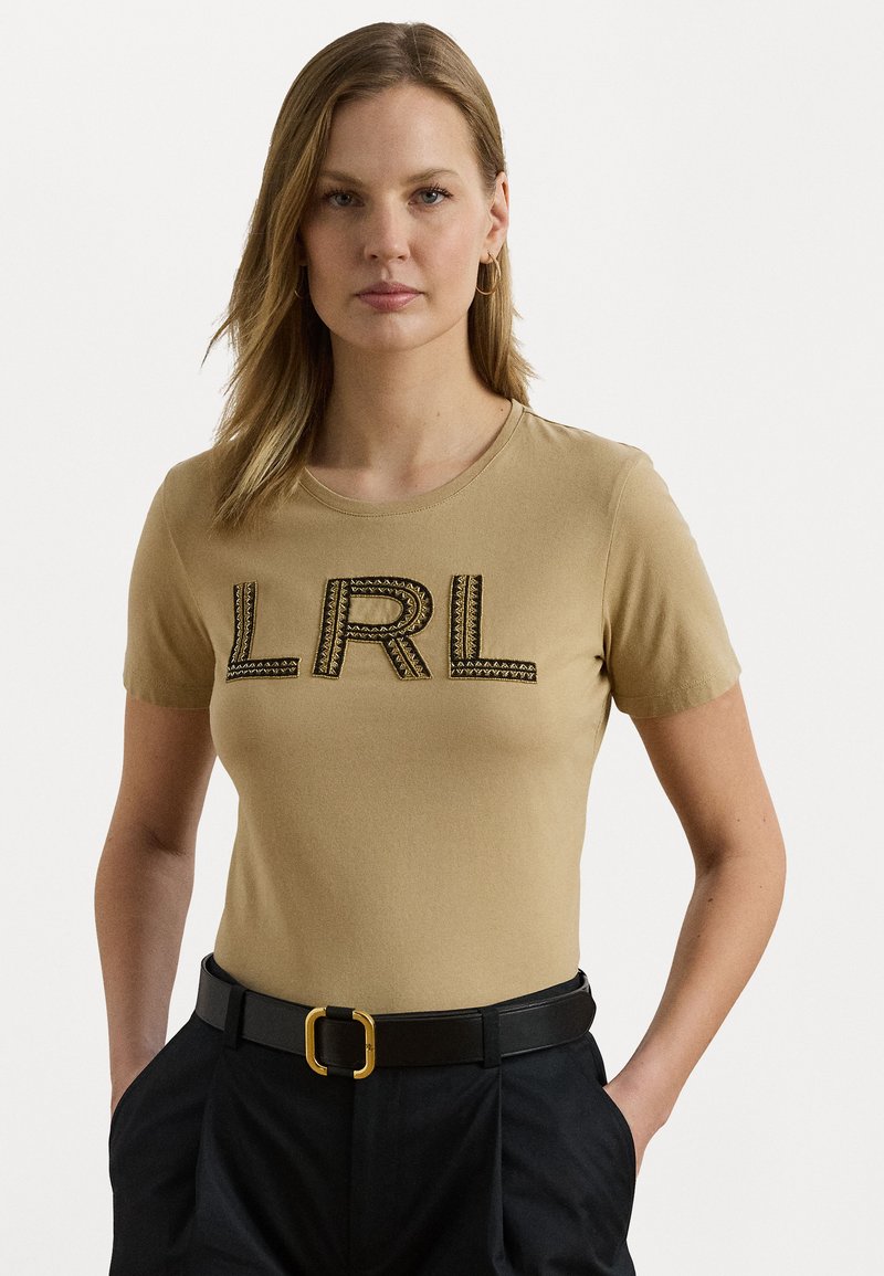 Beige bomull t-skjorte med rund hals, korte ermer og teksturert svart "LRL" bokstaver dekorert med et geometrisk mønster.