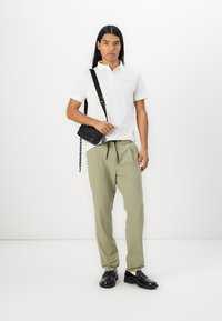 White polo shirt, light green trousers, black crossbody bag, and black shoes. Smooth fabric, slim fit, elastic waistband on pants.