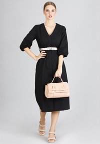 Svart klänning med trekvarts ärm, V-ringning och bältesmidja; kombinerad med en rosa handväska med präglad text och kraftiga sandaler.