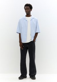 Camicetta a righe a maniche corte in azzurro chiaro e bianco, abbinata a jeans neri a gamba larga e scarpe da ginnastica nere. Design semplice, vestibilità casual.