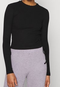 Svart ribbad långärmad topp med rundad halsringning och sidovikningar, parat med mjuka, ljuslila texturerade byxor.