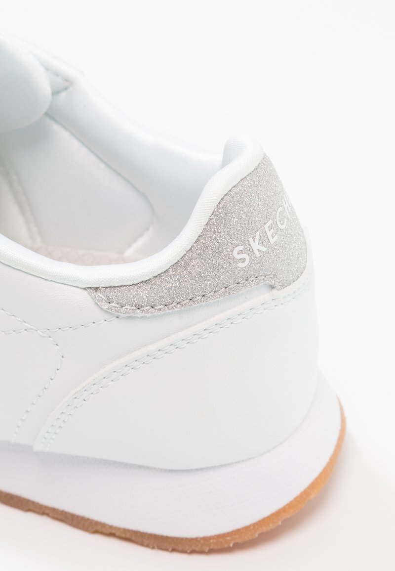 Witte sneaker met een glad leren bovenwerk, een glinsterende zilveren accent bij de hak en een getextureerde inlegzool, met een rubberen buitenzool.