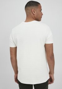 Hvid t-shirt med korte ærmer, der har vandret ribbet tekstur, rund halsudskæring og en let længere bagkant.