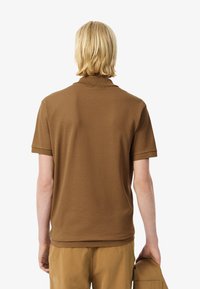 Hnědé polotriko s jemnou texturou, krátkými rukávy a límečkem. Zadní strana je čistě dokončená s jemným detailním švem na lemu.