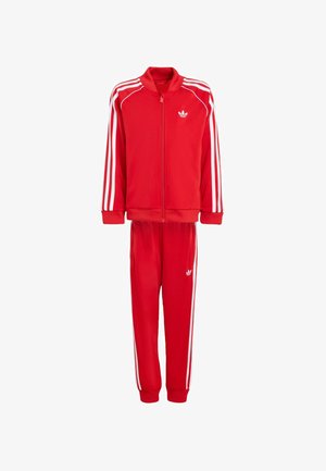 Piros sport melegítő, cipzáras felsővel és hozzá illő nadrággal. Fehér oldalsávokkal és logóval, sima anyagból készült.