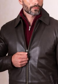 Dark brown leather jacket with a collared neck, zipper front, and ribbed maroon inner layer. Smooth texture and tailored fit.