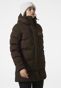 Bruine geïsoleerde jas met een rits aan de voorkant, hoge kraag en logo op de borst. Heeft een capuchon en ritszakken aan de zijkanten.