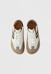 Baskets blanches et grises en cuir et daim, avec un bout rond, des lacets blancs, des accents noirs et une semelle en caoutchouc gomme.