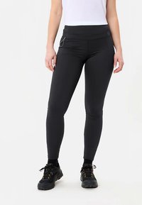 Zwarte legging met een brede tailleband, een gladde textuur en een zijzak met een zilveren ritsdetail, gecombineerd met zwarte sneakers.