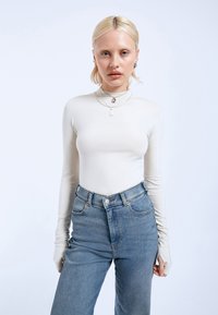 Long-sleeve cream bodysuit with a high neck, paired with light blue high-waisted jeans, featuring subtle fading and a classic five-pocket design.