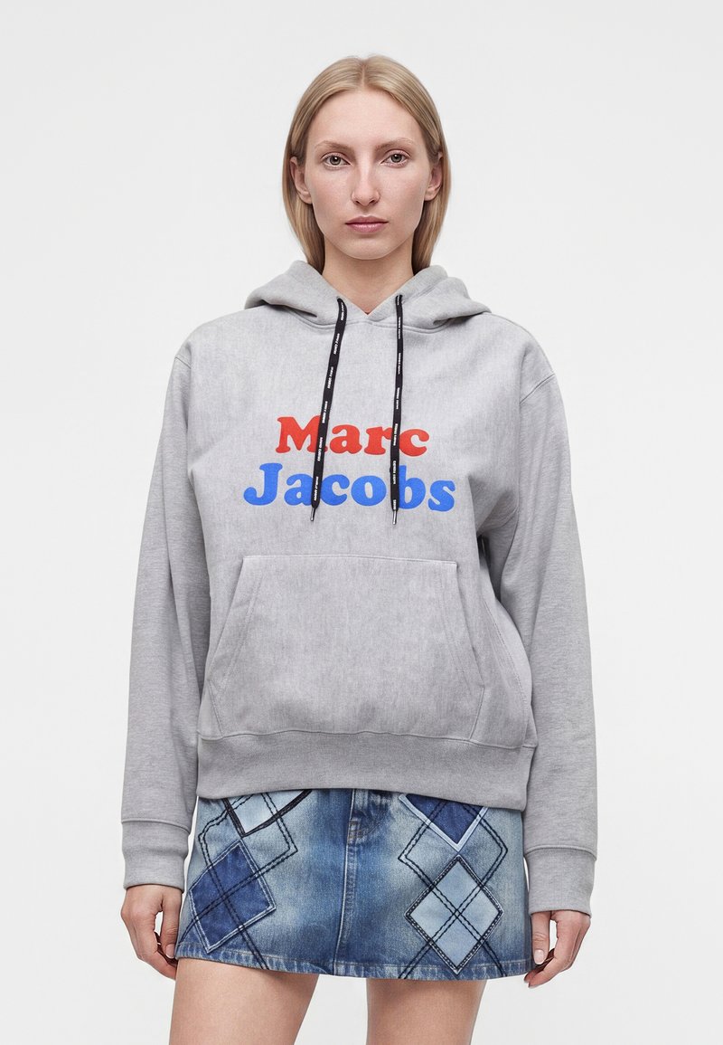 Γυναίκα που φορά γκρι φούτερ Marc Jacobs με κόκκινα και μπλε γράμματα και μπλε τζιν φούστα με κεντήματα διαμαντένιων σχεδίων.